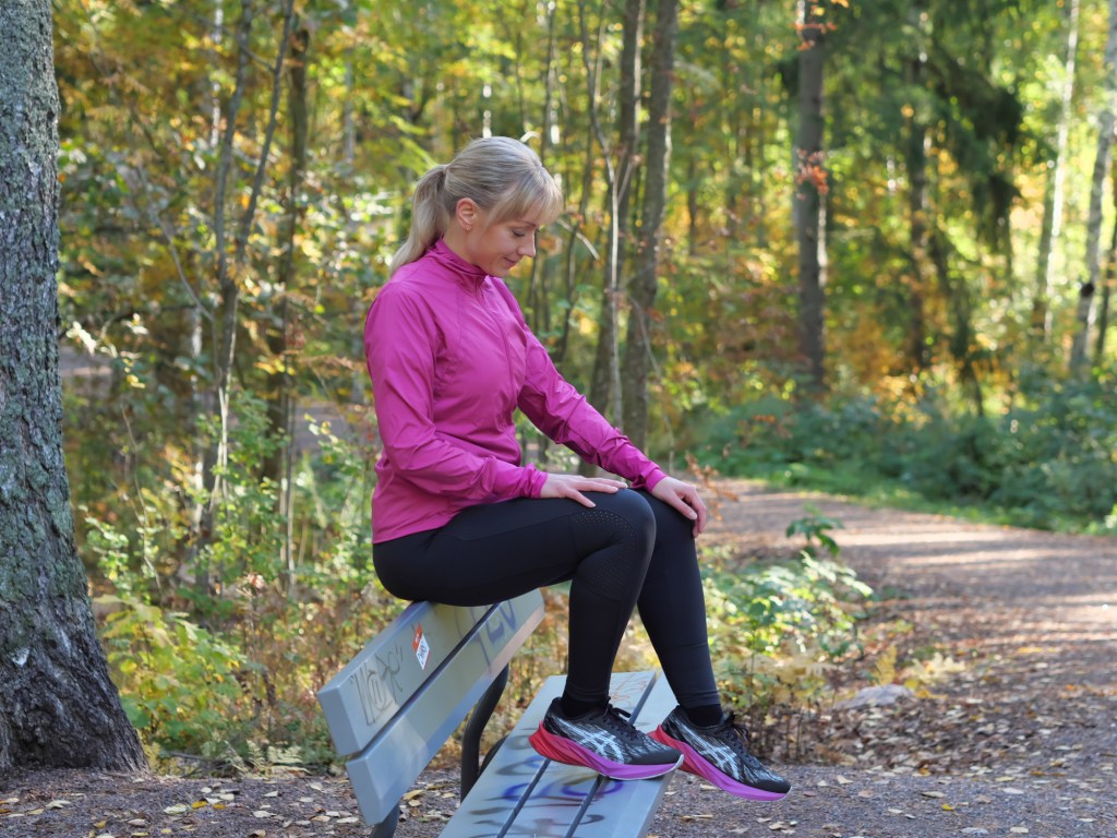 juoksija istuu puiston penkilla ja katsoo jalkoihinsa