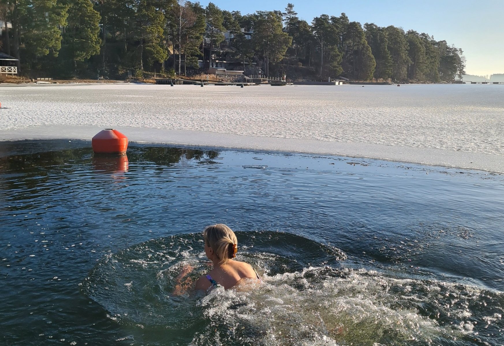 nainen ui avannossa helmikuussa ja aurinko paistaa