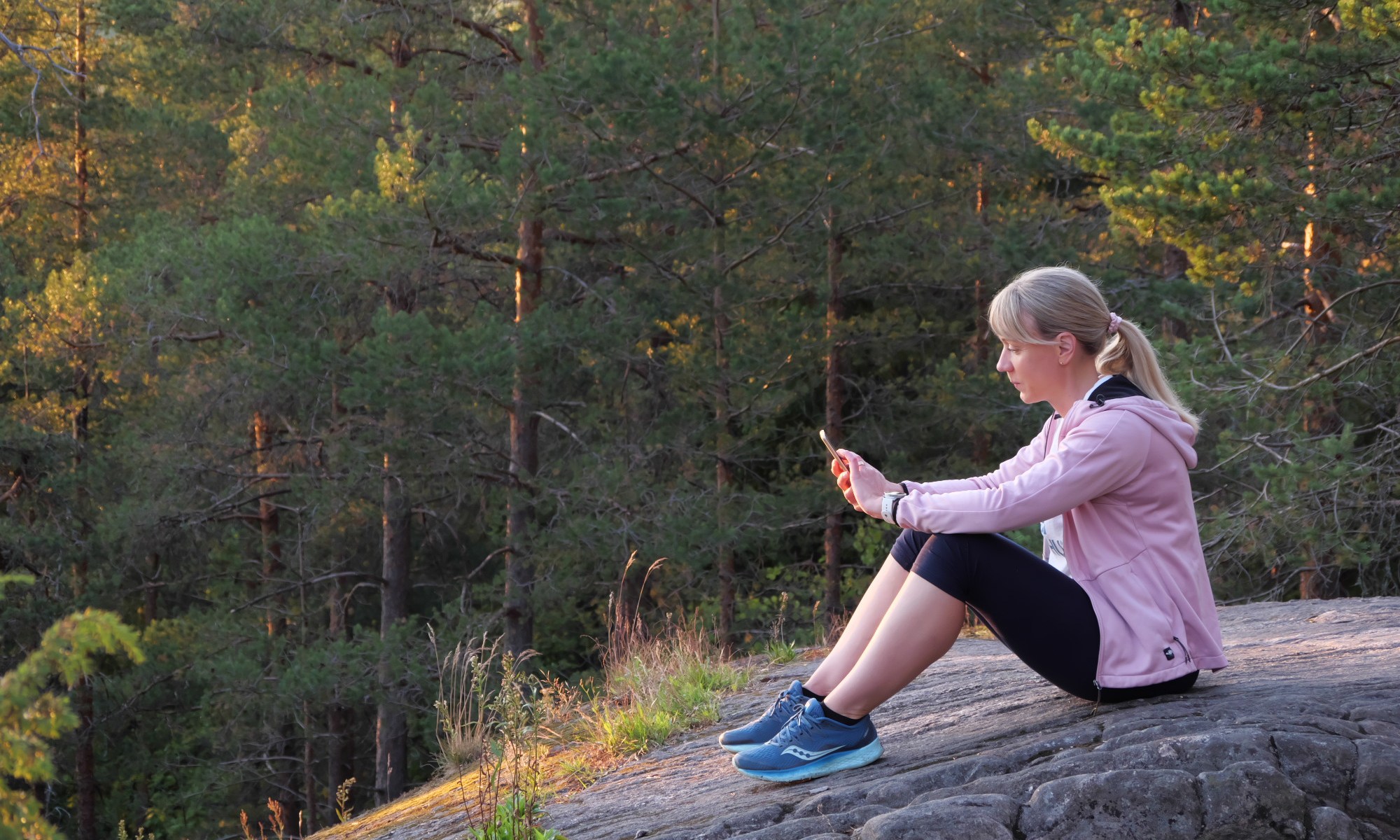 nainen istuu kalliolla ja selaa puhelintaan