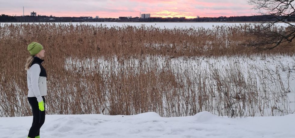 juoksija katselee laskevaa aurinkoa talvella merenrannassa