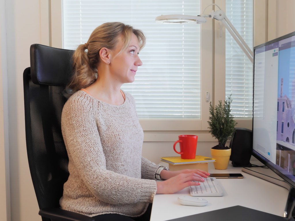 nainen katsoo isoa nayttoa ja kirjoittaa