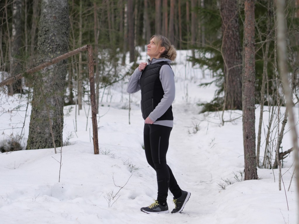 juoksija sulkee tikkiliivin vetoketjua talvisessa metsassa