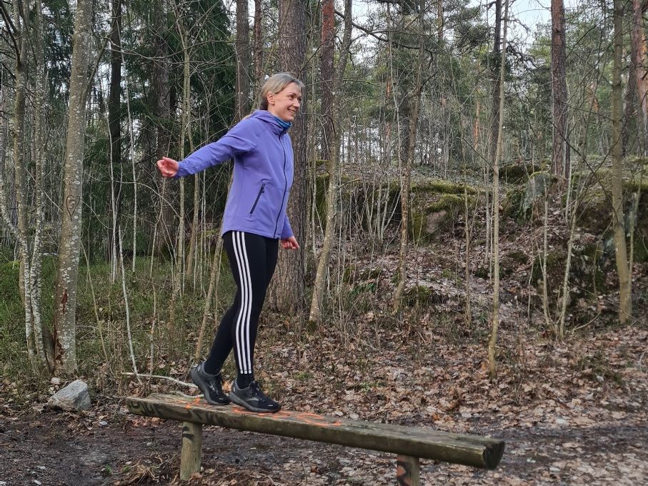 juoksija tasapainoilee puisen penkin paalla ja hymyilee