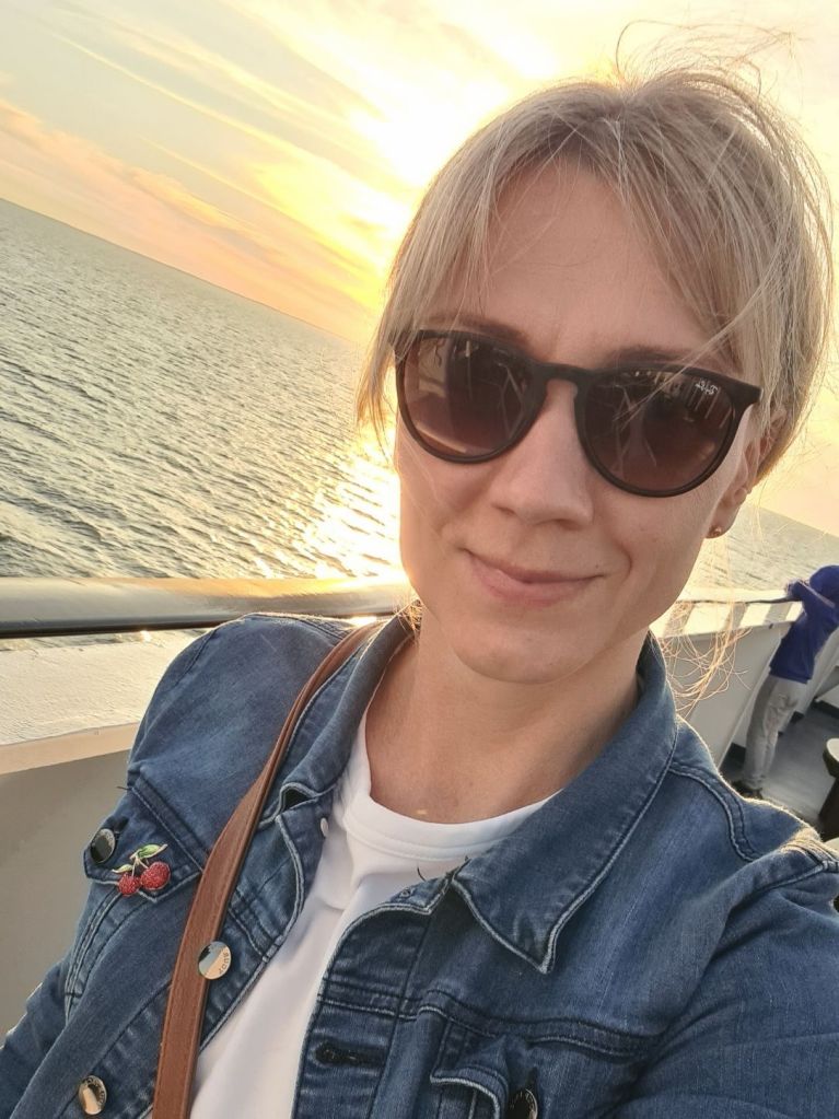 nainen seisoo laivan kannella ja aurinko laskee selan taa