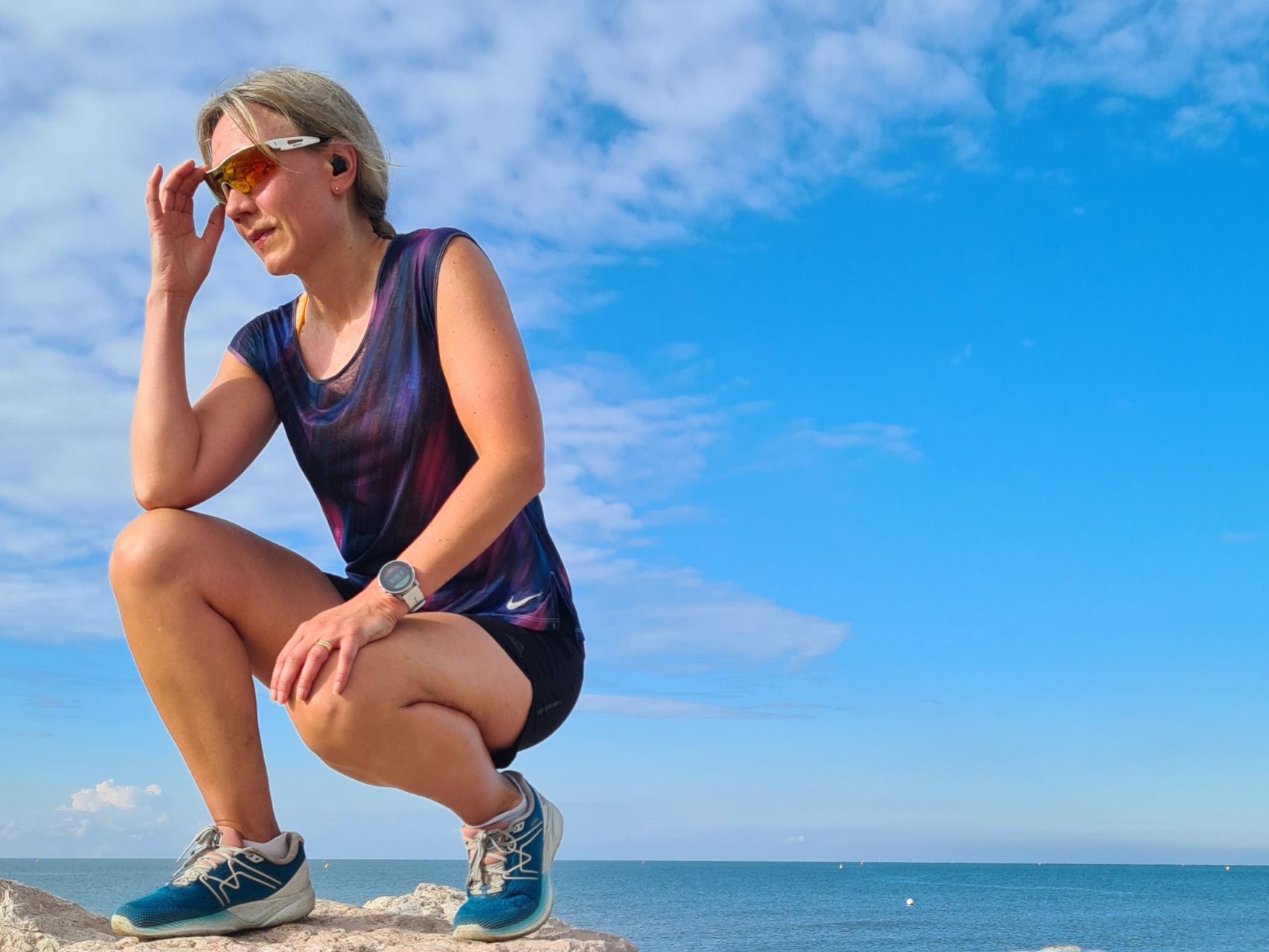 juoksija on kyykyssa rantakivella ja ottaa aurinkolaseja pois