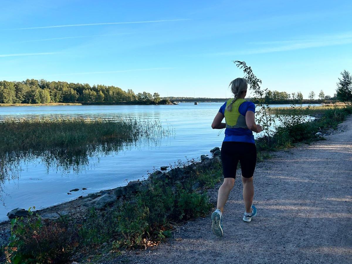 a woman running by the sea with a running vest on