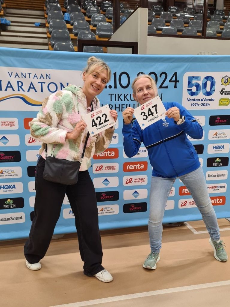 kaksi naisjuoksijaa hymyilee kameralle juoksunumerot kasissaan