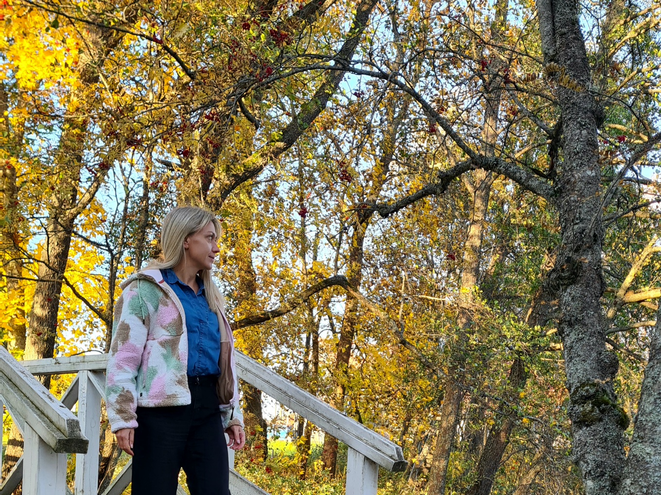 nainen kavelee puusillalla ja puissa on ruska