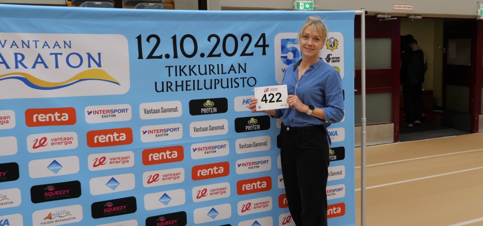 naisjuoksija seisoo mainosjulisteen edessa ja pitelee juoksunumeroaan