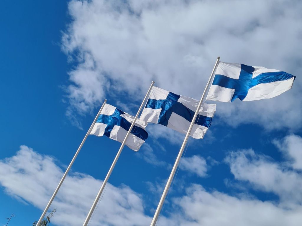 kolme suomen lippua liehuu taivasta vasten