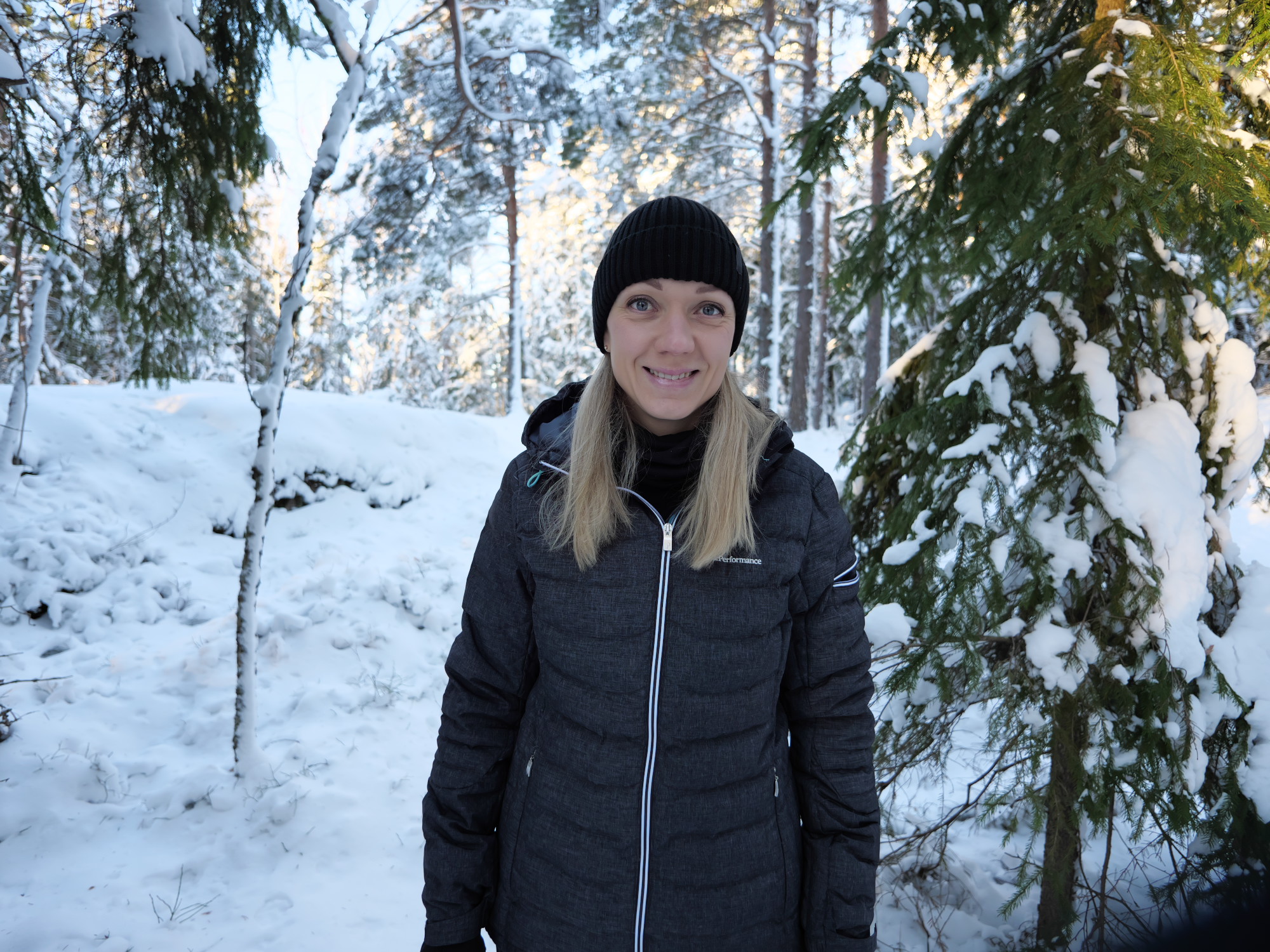 nainen seisoo toppavaatteissa lumisessa metsassa