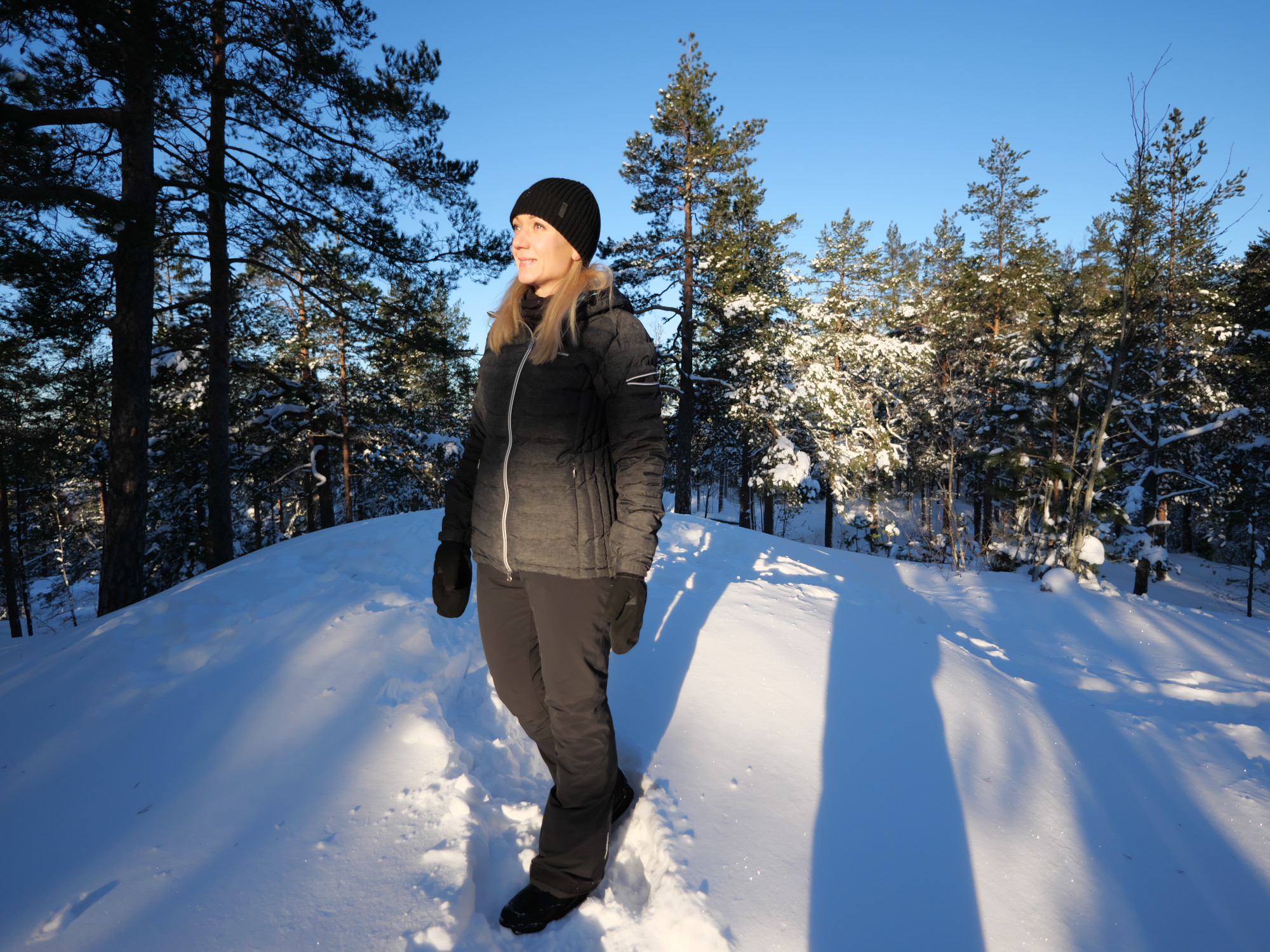 nainen seisoo lumisen kallion paalla ja katsoo kohti aurinkoa