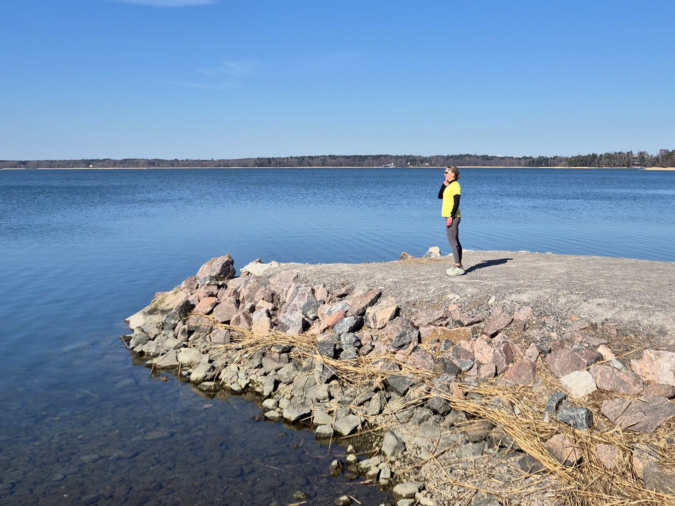 nainen seisoo juoksuvaatteissa ja katsoo merelle