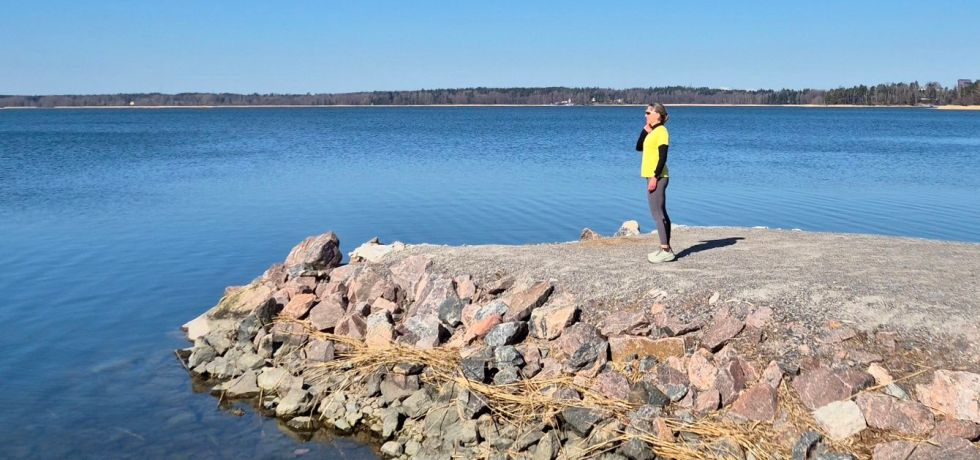 nainen seisoo juoksuvaatteissa ja katsoo merelle