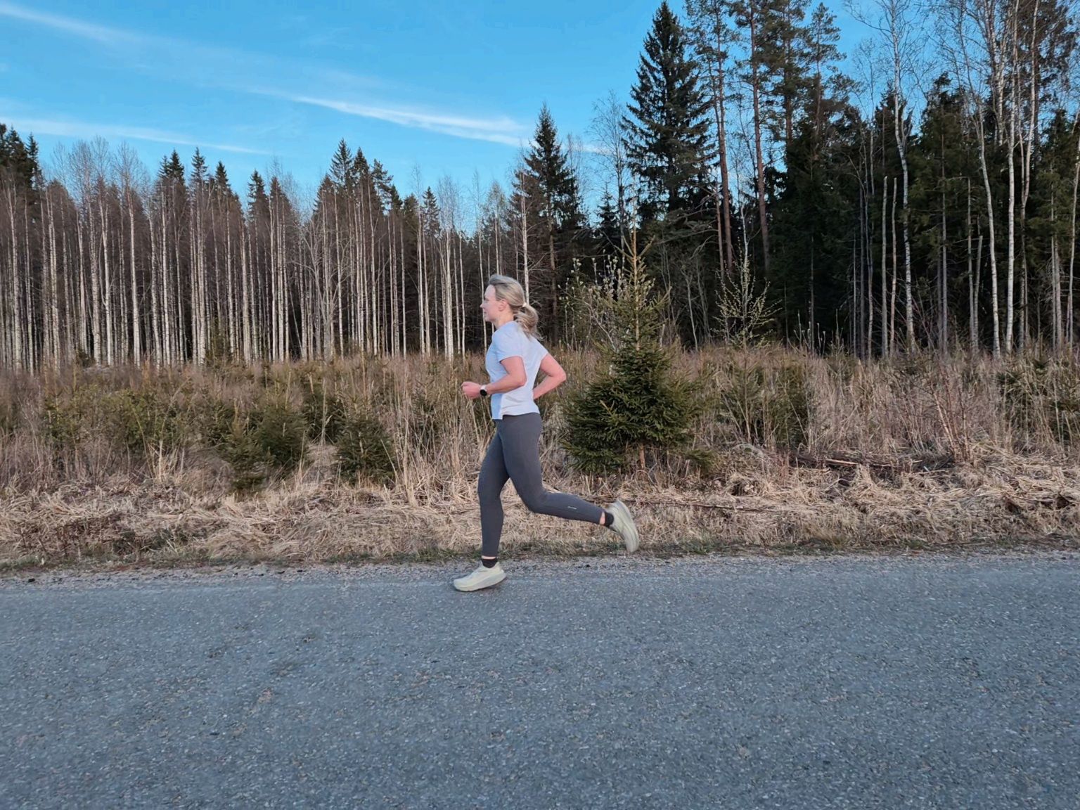 nainen juoksee pitkin asfalttitieta